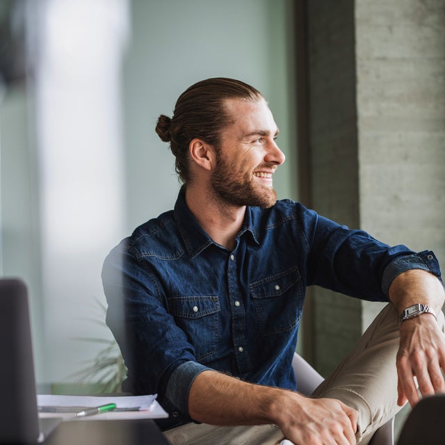 The Image shows a young man with a dark blue shirt, sitting relaxed on a table right by a window on the right side of the picture. He is smiling while looking outside, because with ista, his electricity billing is simplified and still precise, making it an effortless billing experience.